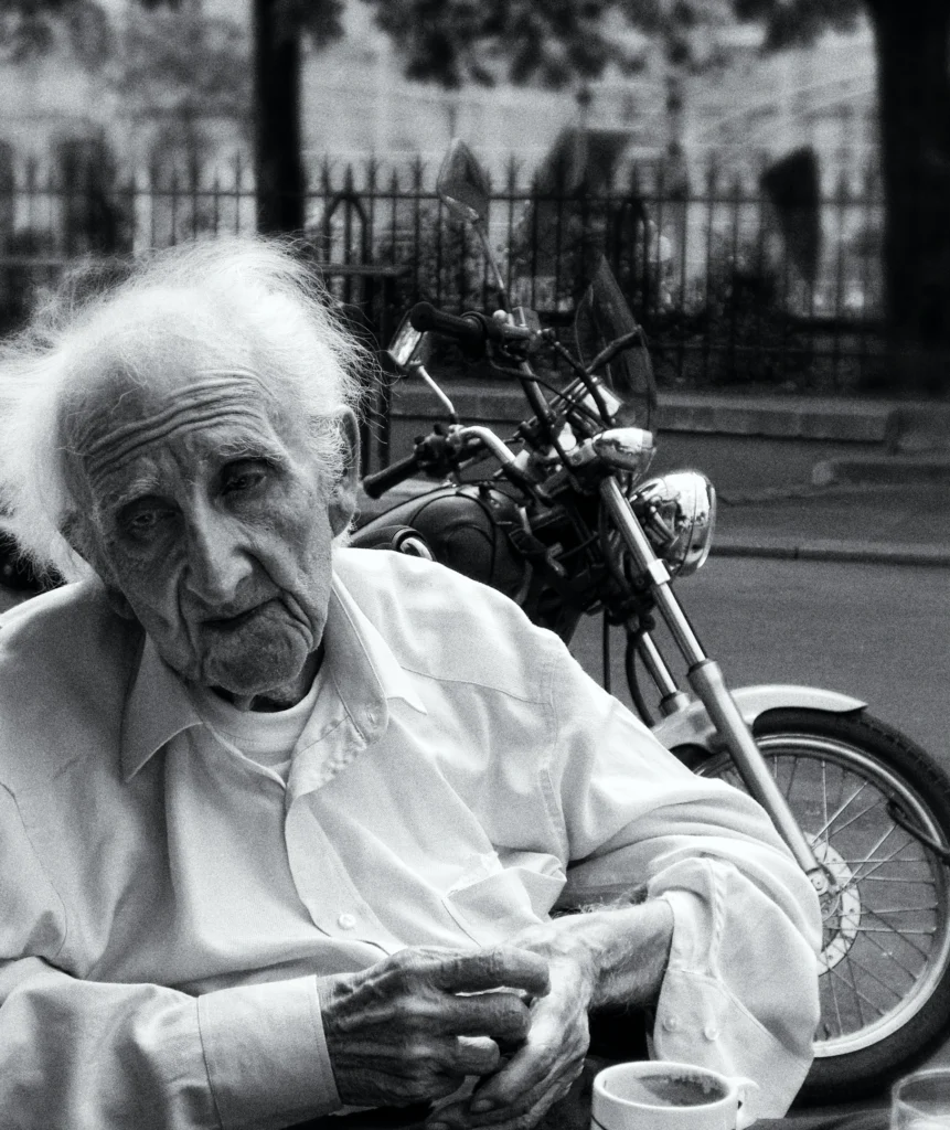Homme plus âgé contemplant la vie, avec une moto derrière lui.